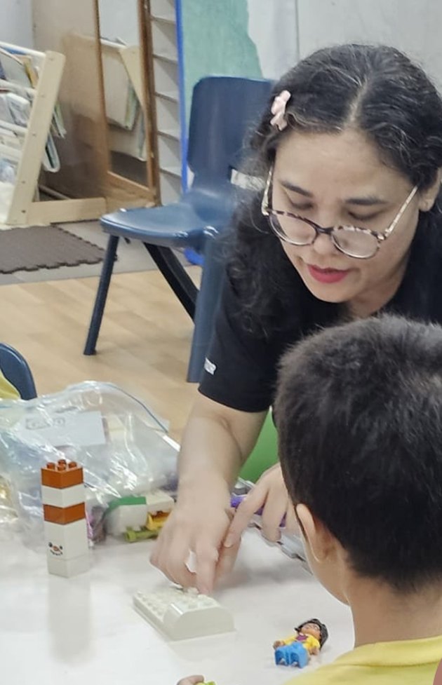Devina leaning over a classroom table, guiding a child through a hands-on coding activity
